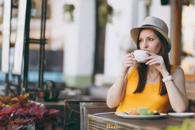 Açık havada sokak kafe Cafe kapuçino, bardak ile sarı kıyafet şapka masada oturan kadın kek, restoranda serbest zaman sırasında rahatlatıcı. Mobil ofis yazında. Yaşam tarzı dinlenme kavramı