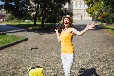 Seyahat etmek turist kadın sarı rahat kıyafetler içinde retro vintage fotoğraf kamera Yayilim açık elele bavulla çok memnun. Hafta sonu kaçamağı yurt kız. Turizm yolculuk yaşam tarzı