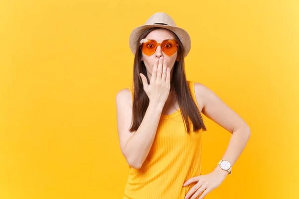 Portrait of shocked fun crazy young woman in straw summer hat, orange glasses put hands on face, copy space isolated on yellow background. People sincere emotions, lifestyle concept. Advertising area