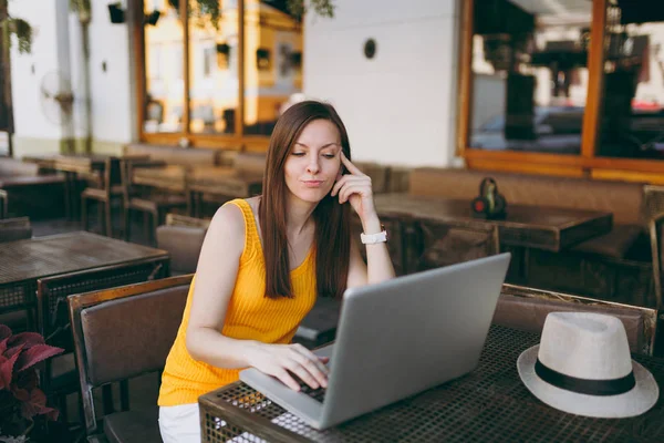 Woman in outdoors street coffee shop cafe sitting at table working on modern laptop pc computer, relaxing in restaurant during free time. Mobile Office in summer. Lifestyle freelance business concept