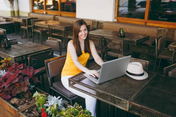 Woman in outdoors street coffee shop cafe sitting at table working on modern laptop pc computer, relaxing in restaurant during free time. Mobile Office in summer. Lifestyle freelance business concept