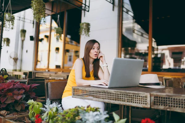 Woman in outdoors street coffee shop cafe sitting at table working on modern laptop pc computer, relaxing in restaurant during free time. Mobile Office in summer. Lifestyle freelance business concept