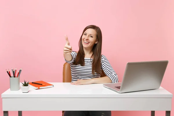 stock image Smiling woman in casual clothes show thumb up sit work at white desk with contemporary pc laptop isolated on pastel pink background. Achievement business career concept. Copy space for advertisement