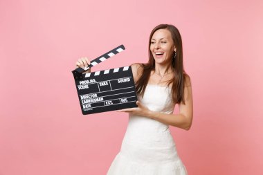 Pastel pembe arka plan üzerinde izole Klaket yapma klasik kara film holding beyaz gelinlik gelin kadın gülen portre. Yapılacaklar listesi düğün. Kutlama organizasyonu. Kopya alanı
