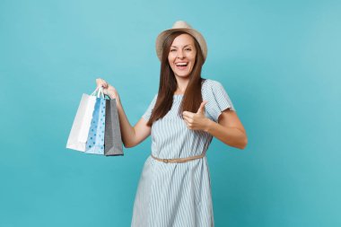 Moda gülümseyen güzel beyaz kadın portre yaz elbise, hasır şapka alışveriş izole mavi pastel arka plan üzerinde sonra paketleri çanta satın almalarla tutarak. Kopya alanı reklam için