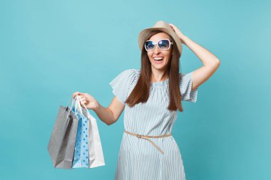 Moda çekici mutlu kadın portre yazlık elbise, hasır şapka, güneş gözlüğü izole mavi pastel arka plan üzerinde alışveriş sonra paketleri çanta satın almalarla tutarak. Kopya alanı reklam için