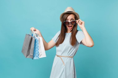 Moda çekici mutlu kadın portre yazlık elbise, hasır şapka, güneş gözlüğü izole mavi pastel arka plan üzerinde alışveriş sonra paketleri çanta satın almalarla tutarak. Kopya alanı reklam için