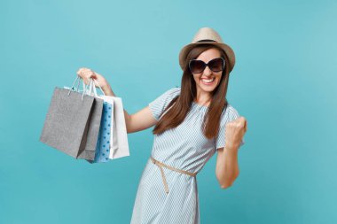 Moda çekici mutlu kadın portre yazlık elbise, hasır şapka, güneş gözlüğü izole mavi pastel arka plan üzerinde alışveriş sonra paketleri çanta satın almalarla tutarak. Kopya alanı reklam için