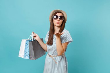 Moda çekici mutlu kadın portre yazlık elbise, hasır şapka, güneş gözlüğü izole mavi pastel arka plan üzerinde alışveriş sonra paketleri çanta satın almalarla tutarak. Kopya alanı reklam için