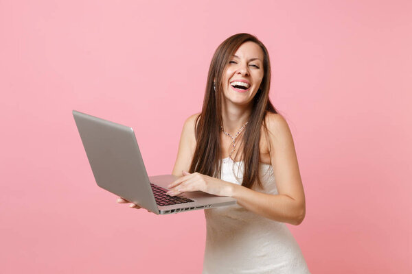 Portrait of laughing happy bride woman in wedding dress planning wedding, working on laptop pc computer isolated on pastel pink background. Wedding to do list. Organization of celebration. Copy space