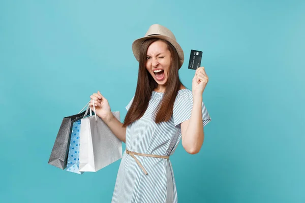 Portrait of beautiful caucasian woman in summer dress, straw hat holding packages bags with purchases after shopping, bank credit card isolated on blue pastel background. Copy space for advertisement