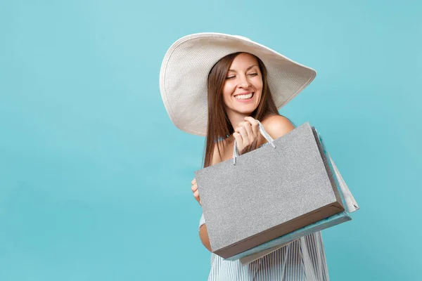 Portrait fashionable elegant fashion beautiful caucasian woman in summer dress, white large wide brim sun hat holding packages bags with purchases after shopping isolated on blue pastel background