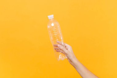 Erkek yakından el şeffaf temizleme boş boş plastik şişe soda su üzerinde sarı arka plan izole için basılı tutun. Ambalaj şablon mockup. Susuzluk hizmet anlayışı. Uzay kopyalayın. Reklam alanı