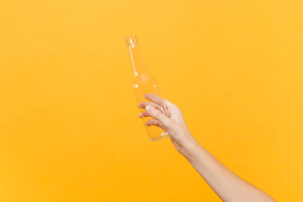 Close up female hold in hand transparent clear empty blank glass bottle for soda cola isolated on yellow background. Packaging template mockup. Delivery service concept. Copy space. Advertising area