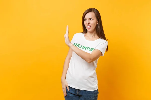 Portrait of sad upset shocked young woman in white t-shirt with written inscription green title volunteer isolated on yellow background. Voluntary free assistance help, charity grace work concept