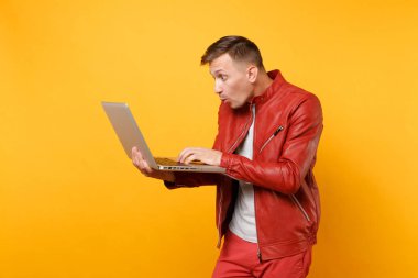 Portre vogue eğlenceli kırmızı deri ceket, t-shirt yakışıklı genç adam dizüstü pc kullanarak tablet üzerinde izole parlak sarı eğilimleri arka plan. İnsanlar samimi duygular yaşam tarzı kavramı. Reklam alanı