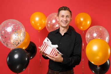 Neşeli genç adam siyah klasik gömlek holding kırmızı kutusunda hediye, parlak kırmızı arka plan hava balonu üzerinde mevcut. Dünya Kadınlar günü, mutlu yeni yıl, Doğum günü mockup tatil parti konsept