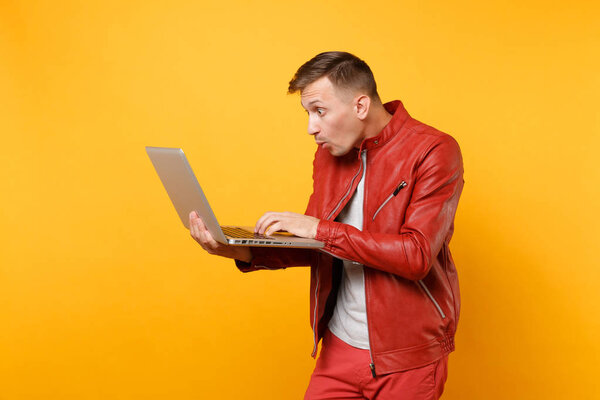 Portrait vogue fun handsome young man in red leather jacket, t-shirt using laptop pc tablet isolated on bright trending yellow background. People sincere emotions lifestyle concept. Advertising area