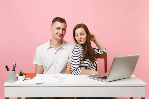 Two young tender business woman man colleagues sit work at white desk with contemporary laptop isolated on pastel pink background. Achievement career concept. Copy space advertising, youth co working