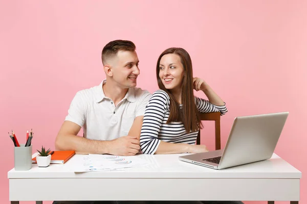 Two young tender business woman man colleagues sit work at white desk with contemporary laptop isolated on pastel pink background. Achievement career concept. Copy space advertising, youth co working