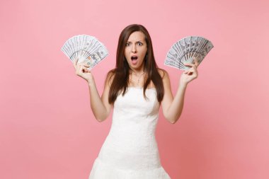 Paket çok dolar, nakit para, pembe arka plan izole holding beyaz gelinlik içinde açılan ağız şok endişe gelin kadınla. Düğün kutlama kavramı organizasyonu. Kopya alanı