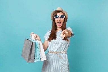 Moda çekici mutlu kadın portre yazlık elbise, hasır şapka, güneş gözlüğü izole mavi pastel arka plan üzerinde alışveriş sonra paketleri çanta satın almalarla tutarak. Kopya alanı reklam için