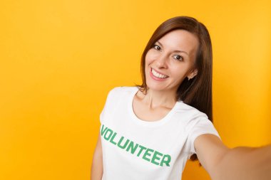 Mutlu gülümseyerek Selfie görüntü izole sarı arka plan üzerinde yazılı yazıt yeşil başlık gönüllü olan beyaz tişört kadında memnun. Gönüllü ücretsiz destek yardım, sadaka grace iş kavramı