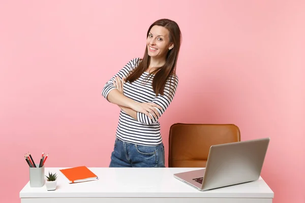 Young beautiful girl in casual clothes work, standing near white desk with contemporary pc laptop isolated on pastel pink background. Achievement business career concept. Copy space for advertisement