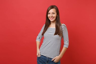 Ayakta, parlak kırmızı duvar arka plan üzerinde izole ceplerinde elele çizgili kıyafetler içinde gülümseyen güzel genç kadın portresi. İnsanlar samimi duygular, yaşam kavramı. Kopyalama alanı alay