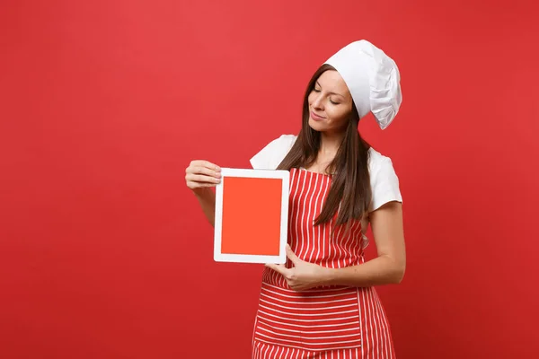 Housewife female chef cook or baker in striped apron white t-shirt toque chefs hat isolated on red wall background. Woman hold tablet blank screen for promotional content Mock up copy space concept