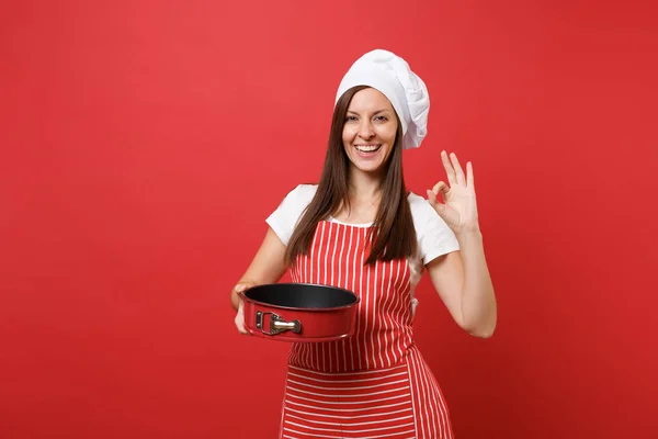 主婦女性シェフや赤い壁の背景に分離された縞のエプロン シャツ トーク シェフ帽子パン屋 パイのため金属製のベーキング フォームを保持している家政婦の女性 コピー スペース コンセプトをモックアップします — ストック写真