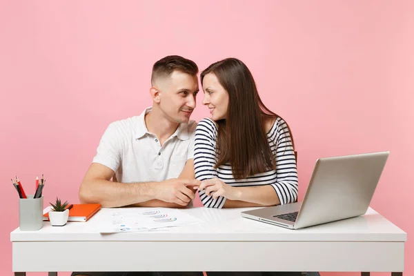 Two young tender business woman man colleagues sit work at white desk with contemporary laptop isolated on pastel pink background. Achievement career concept. Copy space advertising, youth co working