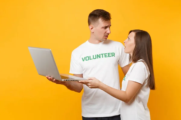 Colleagues couple in white t-shirt with inscription green volunteer using typing laptop pc computer isolated on yellow background. Voluntary free work, assistance help, charity grace teamwork concept