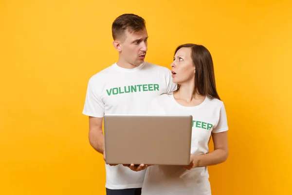 Colleagues couple in white t-shirt with inscription green volunteer using typing laptop pc computer isolated on yellow background. Voluntary free work, assistance help, charity grace teamwork concept