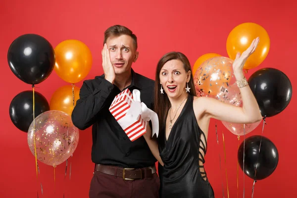 不开心的情侣在黑色的衣服举行礼品盒庆祝生日假期派对在明亮的红色背景气球 情人节国际妇女节快乐新年概念 — 图库照片