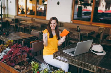 Açık havada sokak kafe modern dizüstü pc bilgisayar ile masada oturan kadın elinde banka kredi kartı, pasaport, kitap online uçak bileti tutun. Serbest zaman restoranda. Yaşam tarzı iş kavramı