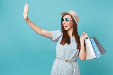 Moda çekici mutlu kadın portre yazlık elbise, hasır şapka, güneş gözlüğü izole mavi pastel arka plan üzerinde alışveriş sonra paketleri çanta satın almalarla tutarak. Kopya alanı reklam için