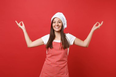 Ev hanımı kadın şef aşçı ya da baker çizgili önlük beyaz t-shirt, toque Şefler Şapka kırmızı duvar arka plan üzerinde izole. Temizlikçi kadın tutmak gülümseyen yoga hareketle eller. Kopyalama alanı kavramı alay