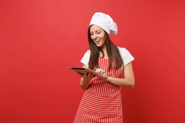 Ev hanımı kadın şef aşçı ya da baker izole kırmızı duvar arka plan üzerinde çizgili önlük, beyaz tişört, toque şefler şapkalı. Eğlenceli kahya kadın tablet pc tarifi arıyorum. Kopyalama alanı kavramı alay