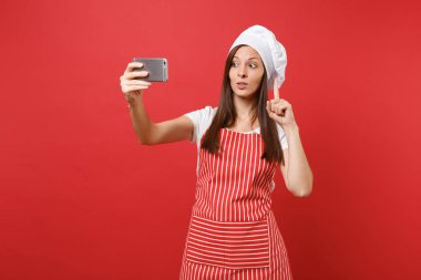Ev hanımı kadın şef aşçı ya da baker izole kırmızı duvar arka plan üzerinde çizgili önlük, beyaz tişört, toque şefler şapkalı. Eğlence gülümseyen kadın selfie cep telefonu üzerinde atış yapıyor. Kopyalama alanı kavramı alay