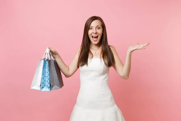 在白色婚礼礼服的兴奋新娘妇女张开手持有多色包袋与购买后查出的粉红色蜡笔背景的购物 婚礼概念的组织 复制空间 — 图库照片