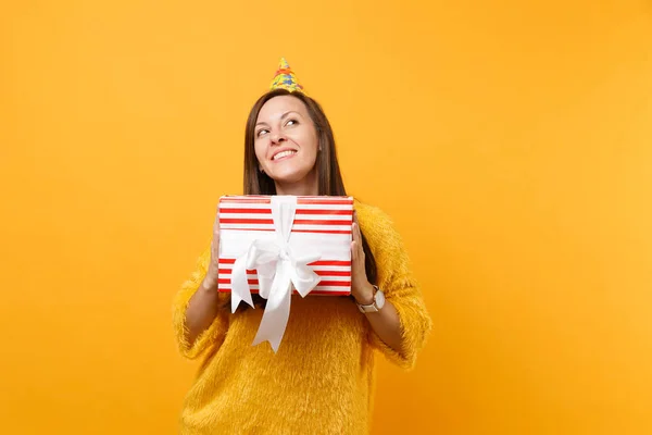 見上げる誕生日帽子で夢のような若い女性は 明るい黄色の背景に分離されて楽しんで休日を提示贈り物に赤い箱を持ってします の心から感情 ライフ スタイルのコンセプト 広告エリア — ストック写真