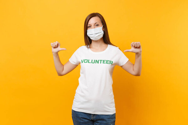 Portrait of woman in white sterile face mask, t-shirt with written inscription green title volunteer isolated on yellow background. Voluntary free assistance help, charity grace work health concept