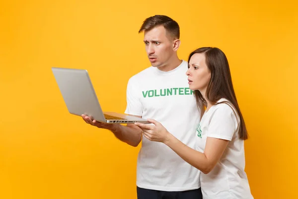 Colleagues couple in white t-shirt with inscription green volunteer using typing laptop pc computer isolated on yellow background. Voluntary free work, assistance help, charity grace teamwork concept