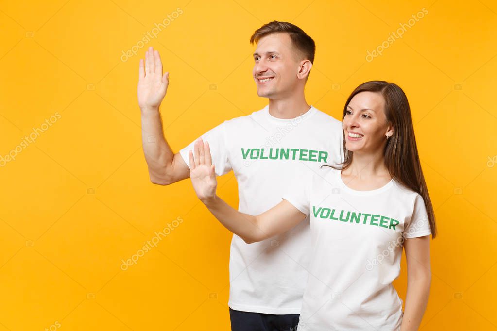 Portrait of young colleagues couple in white t-shirt with written inscription green title volunteer isolated on yellow background. Voluntary free work, assistance help, charity grace teamwork concept