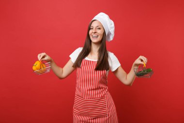 Ev hanımı kadın şef aşçı baker şapkalı izole kırmızı duvar arka plan üzerinde çizgili önlük beyaz t-shirt toque şefler. Kadın tutun sarı biber salatalık bakkal itme arabası sahte kopya alanı kavramı kadar
