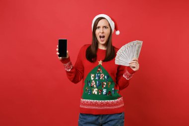 Noel Baba kız kırmızı zemin üzerine izole boş boş ekran ile çok avuç dolar banknotlar, nakit para, cep telefonu tutan tahriş olmuş. Mutlu yeni yıl 2019 kutlama tatil parti konsept