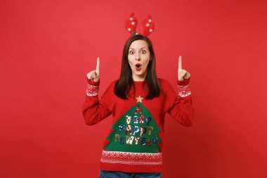 Heyecanlı Noel Baba kız dekoratif geyik boynuzları ağız açık tutarak kafasına işaret parmakları işaret eden oktan yukarı izole kırmızı zemin üzerine. Mutlu yeni yıl 2019 kutlama tatil parti kavramı. Kopyalama alanı alay