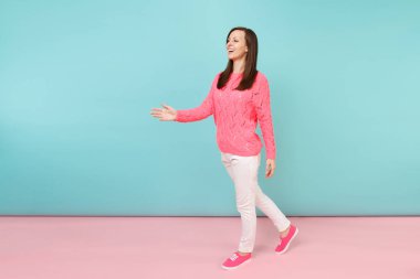 Tam uzunlukta örme gül kazaklı gülümseyen genç kadın portresi, beyaz parlak pembe mavi pastel duvar arka planda Studio izole poz pantolon. Moda yaşam tarzı kavramı. Kopyalama alanı alay