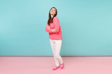Tam uzunlukta örme gül kazaklı gülümseyen genç kadın portresi, beyaz parlak pembe mavi pastel duvar arka planda Studio izole poz pantolon. Moda yaşam tarzı kavramı. Kopyalama alanı alay
